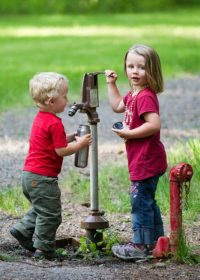 Afbeelding van 2 kinderen die water uit een waterpomp tappen in een Klean Kanteen rvs fles